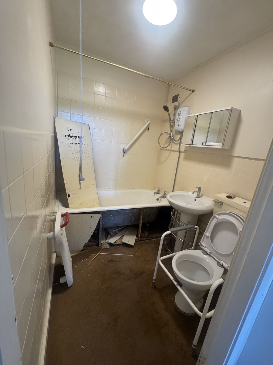 Dated bathroom before renovation, bath removed and floor stripped