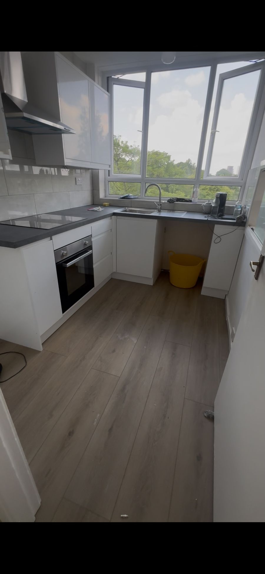 Same kitchen refitted with white units, dark worktop and wood-effect flooring