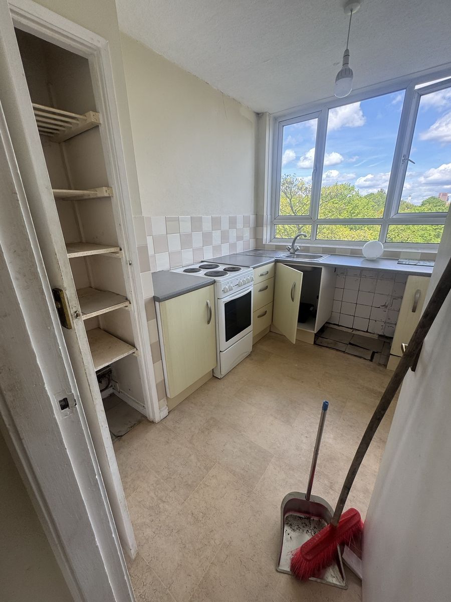 Tired flat kitchen with old cream units and worn vinyl flooring