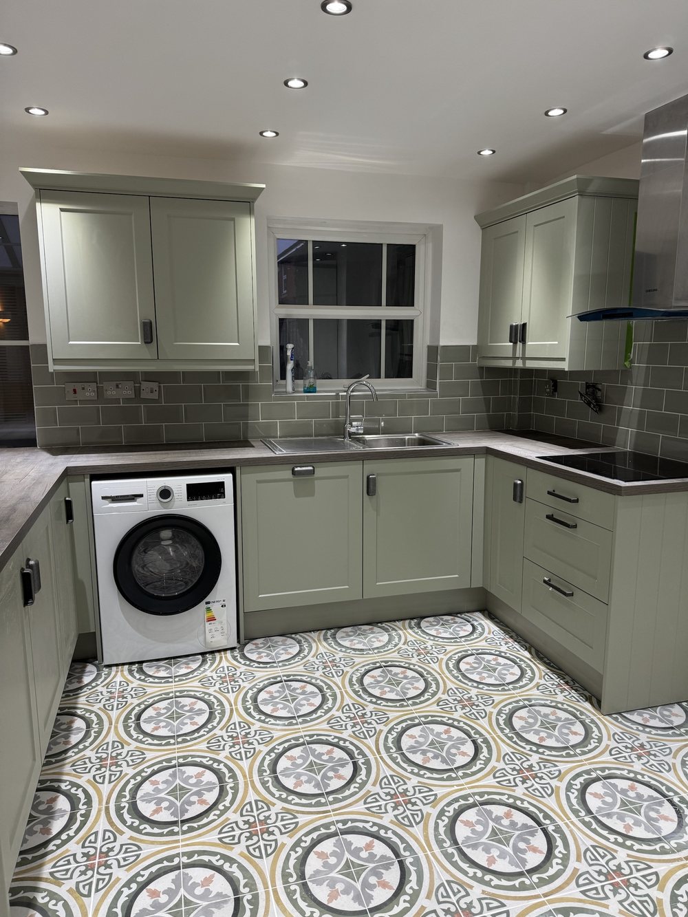 Finished sage green shaker kitchen with tiled splashback, wood-effect worktop, integrated appliances and patterned floor tiles